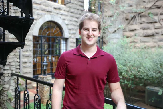 MBA student Josiah Shelley smiling while leaning on a black railing in front of an old looking stone building