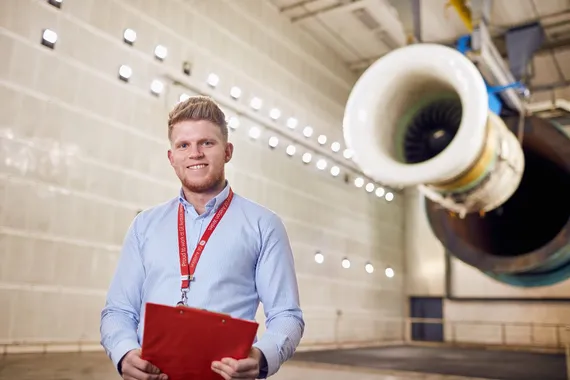 Joshua Stucky, AME graduate and GE employee, is stood wearing a lanyard and holding a clipboard in an aircraft engineering work environement.
