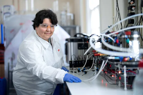 Dr Sandra Esteves is sat in a science facility wearing gloves, a lab coat and safety glasses.