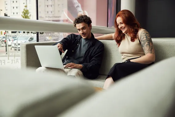 Two students sat on a sofa looking at a laptop.