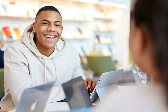 A student smiling and working in the library with a friend.