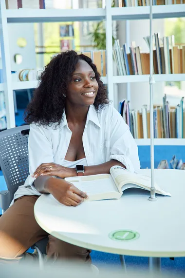 A student sat at a table with a book looking into the distance.