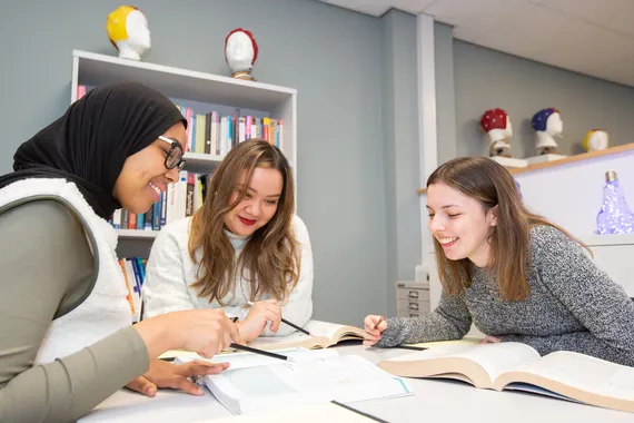 Students smiling and pointing at a text book in the psychology study area.