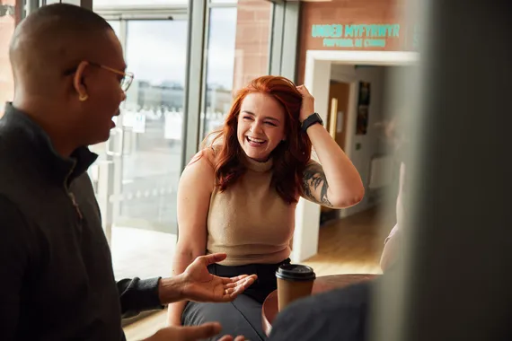 Two students sat smiling and talking in Cardiff campus.
