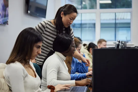 Lecturer surveying students in the Trading Room, accounting data is displayed on the classroom board.