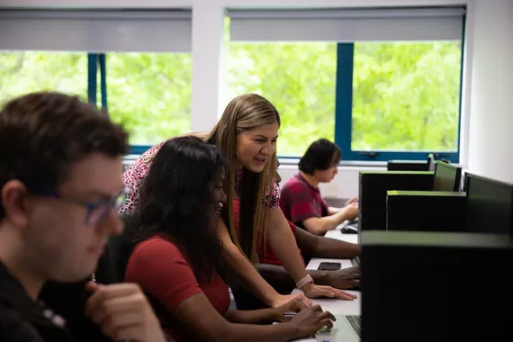 Students working on computers with the help of a lecturer