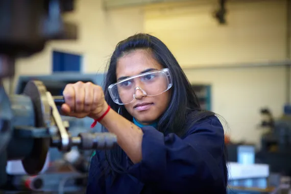 A student is focusing on a peice of machinery, they are wearing eye protection glasses.