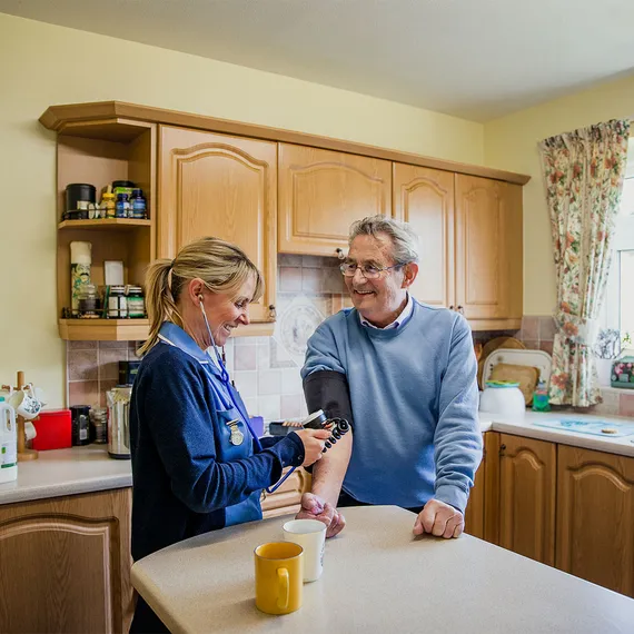 A nurse is taking the blood pressure of an older man in his home.