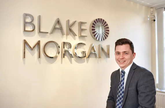 A USW law graduate standing in front of the Blake Morgan logo