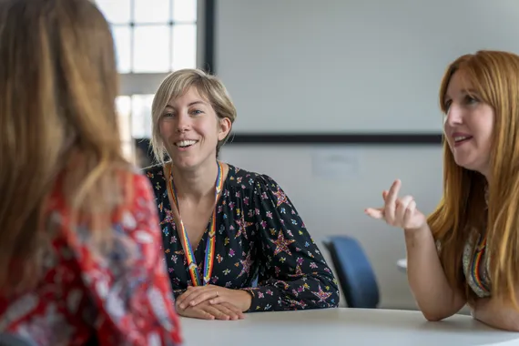 three people are sat around a table having a discussion.