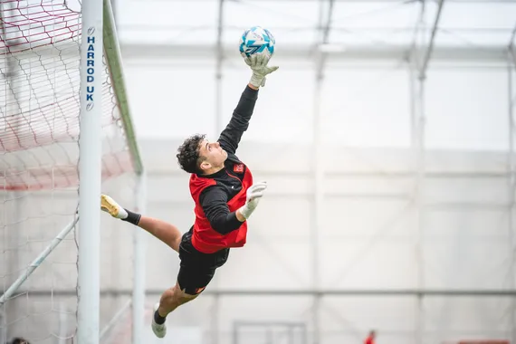 A student is leaping sideways to save a football from entering the goal.