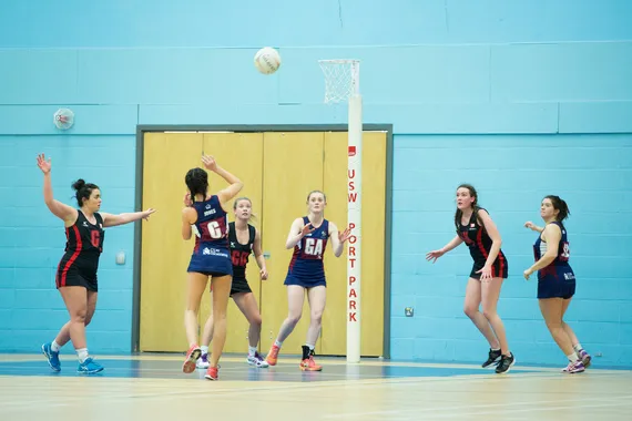 Two teams are playing netball close to the goal.