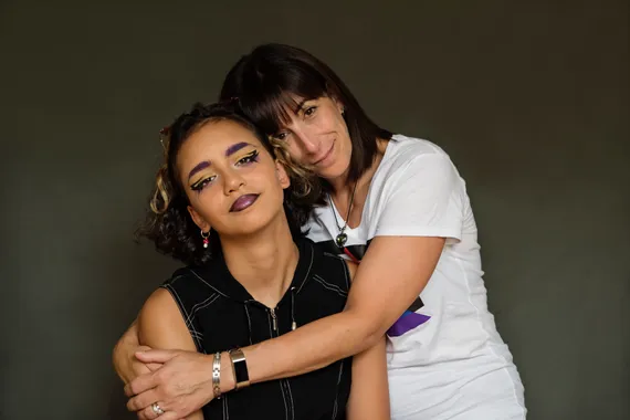 Non-binary teenager and supportive mother smiling at camera