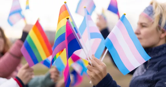 A young person holds a variety of LGBTQ+ flags, including the rainbow Pride flag, the transgender flag and the bisexual flag, while at a Pride march