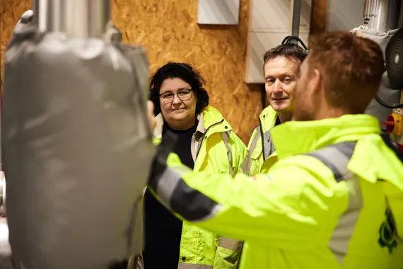 Two USW SERC researchers dressed in high visibility jackets talk to an external research partner also dressed in a high vis jacket while surrounded by machinery at GP Biotec in Powys