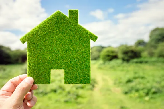 A person holding a felt cut out of a green home with fields behind