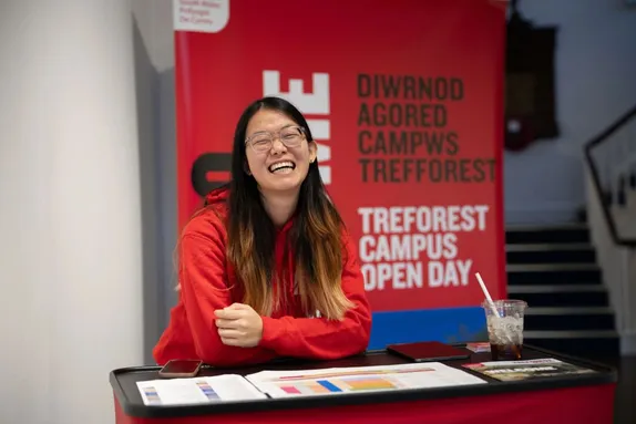 A smiling student ambassador sat at an information stand at a USW open day.