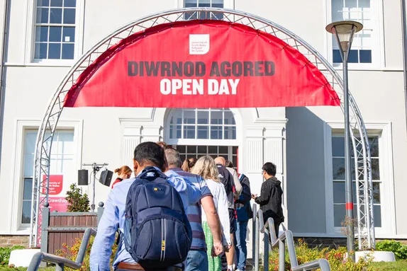 Visitors walking towards the entrance of the USW Treforest campus to check in at the open day. There is a large red banner that reads 'Diwrnod Agored. Open Day'.