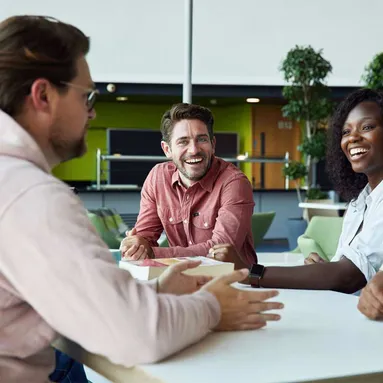 A group of student sitting at a table laughing and talking, one student is looking at the camera