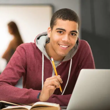 Student smiling at camera while working on their laptop and writing notes