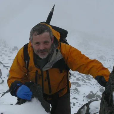 Professor Duncan Pirrie smiling at the camera whilst climbing a snowy mountain.