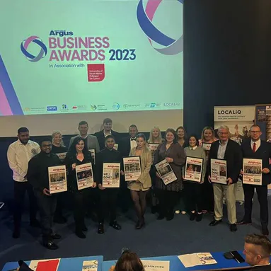 A group of people holding business awards with the South Wales Argus and University of South Wales logos in the backgroud