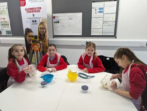 A group of young girls wearing red uniform sitting around a table with jugs and bowls on