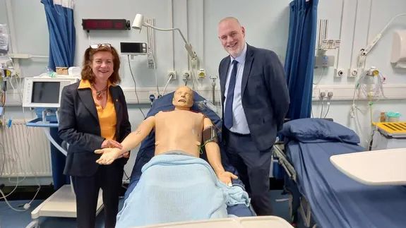 Two individuals (Eluned Morgan on the left and Ben Calvert on the right) standing beside a mannequin in a hospital setting.