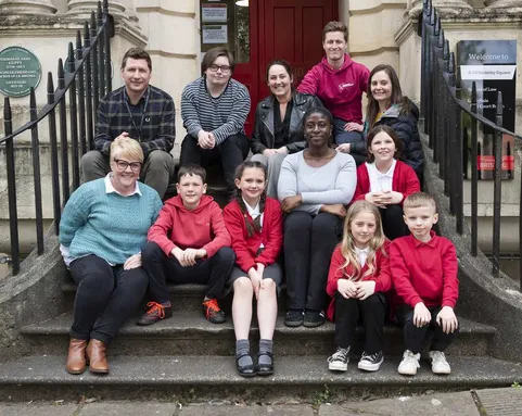 Students sat in red uniforms on steps. Staff and USW colleagues are among them. All are looking at the camera and smiling.
