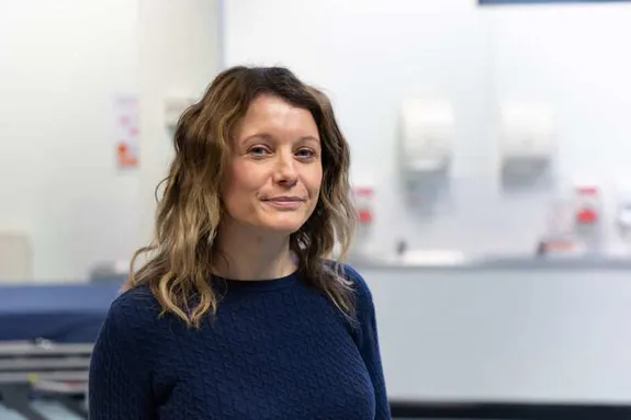 A woman standing in a hospital room, smiling at the camera.