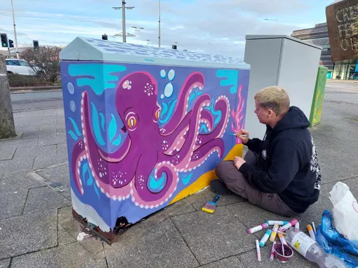 Blake McGauley paints his octopus design onto a electrical box in Cardiff Bay