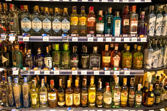 Three shelves in a retail outlet. Each shelf is stacked full of various bottles of alcohol.
