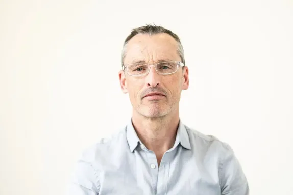 A man with short grey hair, glasses, and light skin.