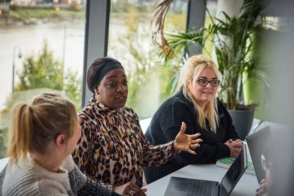 3 women stat around a table taking