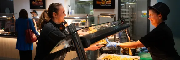 Customer receiving food at Stilts cafeteria on Treforest campus, with various hot dishes displayed on a serving counter under a glass shield.