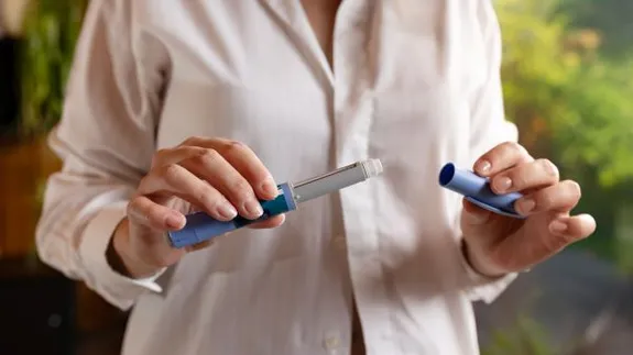 Close-up of a person holding a medication injection pen, with one hand removing the pen cap and the other holding the injector, suggesting preparation for a self-administered injection.