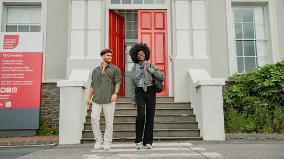 Two people walking down the front steps on campus.