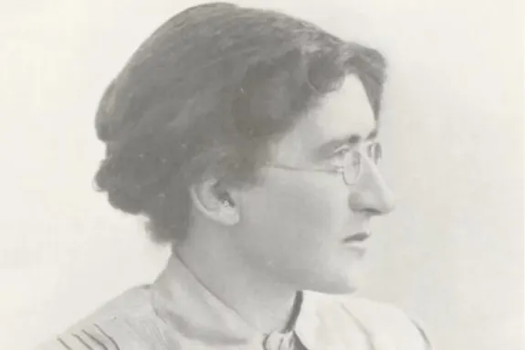 An old photographic portrait of a woman. She is wearing glasses and has long hair that is pinned up.