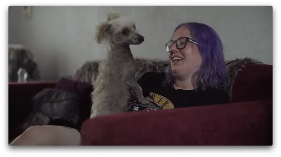 A person is sat on a sofa, smiling, with a dog on their lap.
