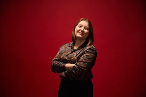 Computing graduate, Niamh, stands for a profile photo in front of a red backdrop