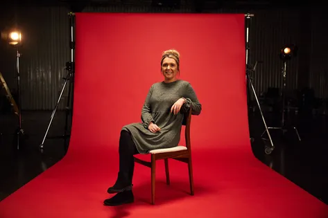 Psychology alumni, Kate, sat on a chair in front of red backdrop