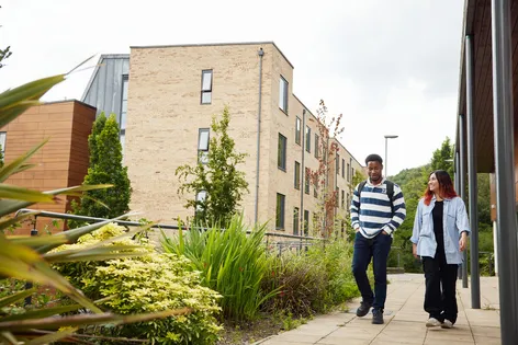 Two students walking past the accommodation buildings and talking.