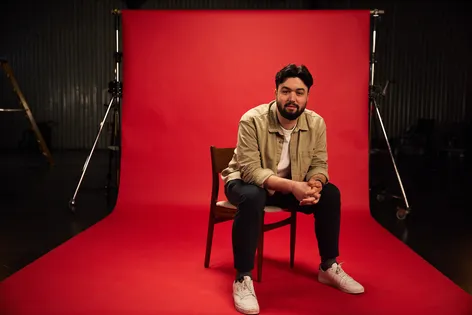 cyber security student savva, sitting on a black chair against our red background