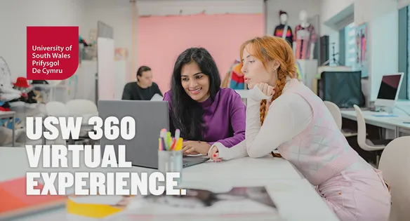 Two students are sat at a table in a fashion studio looking at a laptop together.