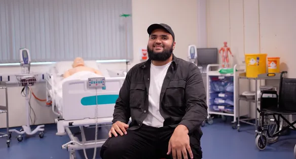 Abdullah is sat in a simulated hospital environment, smiling at the camera.