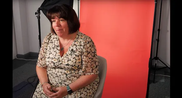 Head of Admissions, Kathryn, is being filmed in front of a red backdrop. There are filming lights in the background.