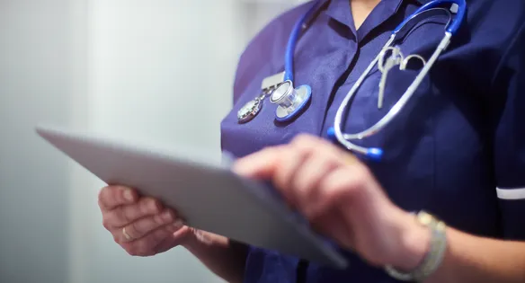 A close up shot of a nurse, wearing scrubs and a stethoscope, looking at information on an iPad.