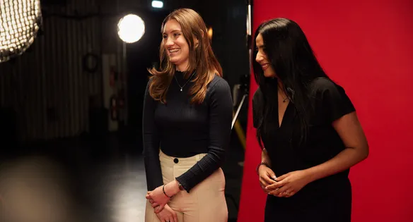 Business graduates, Aakshi and Agnelle, laughing in front of red backdrop