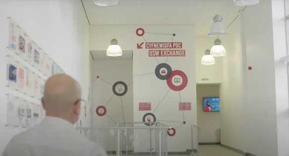 A man is walking through the foyer of the USW business school. The walls have a variety of icons stuck on them to represent the USW Exchange which is printed in bold at the top of the wall.