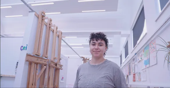 Creative and Therapeutic Arts student, Eugenia, is smiling at the background. There is artwork on the walls behind.